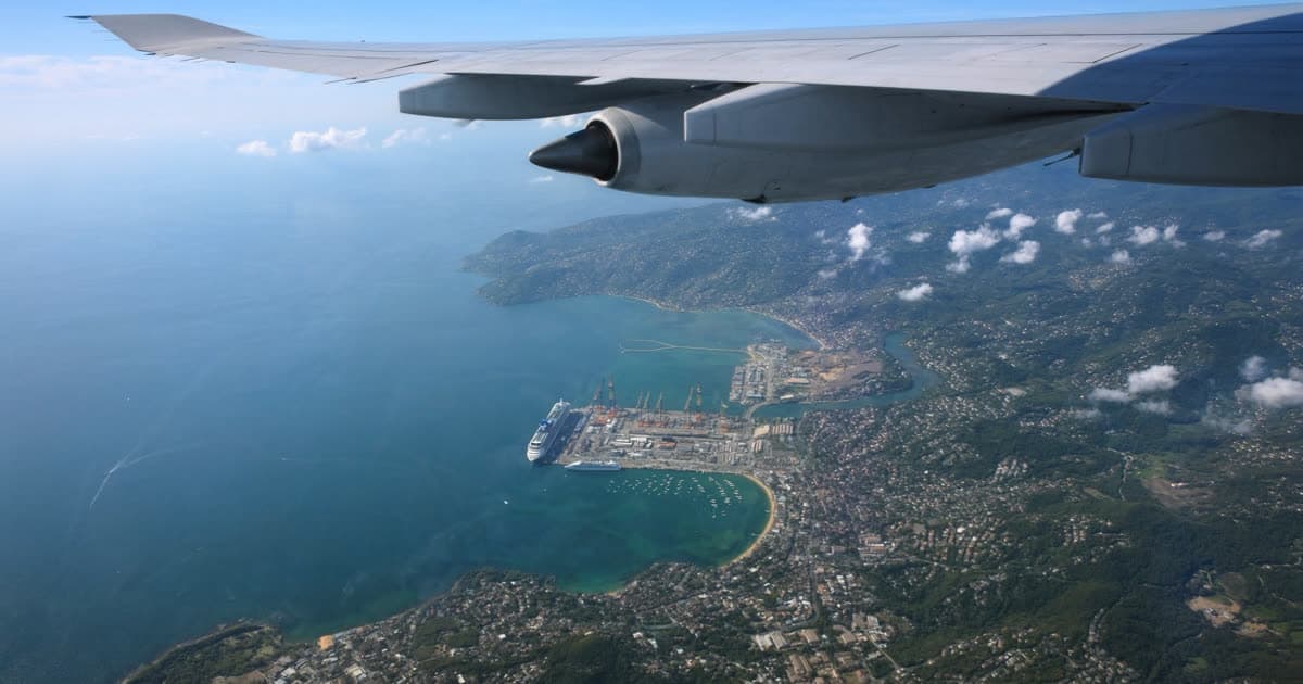 An aircraft descending toward a port city with a ship below