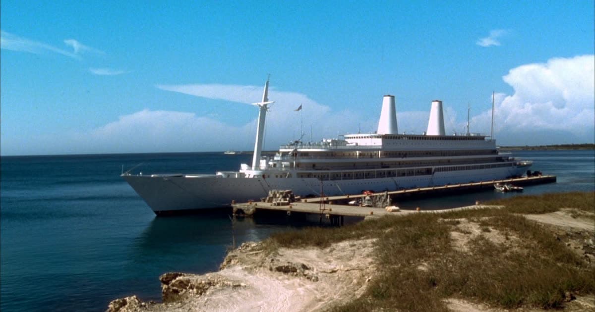 A Disney style cruise ship with twin funnels approaching a Bahamian island