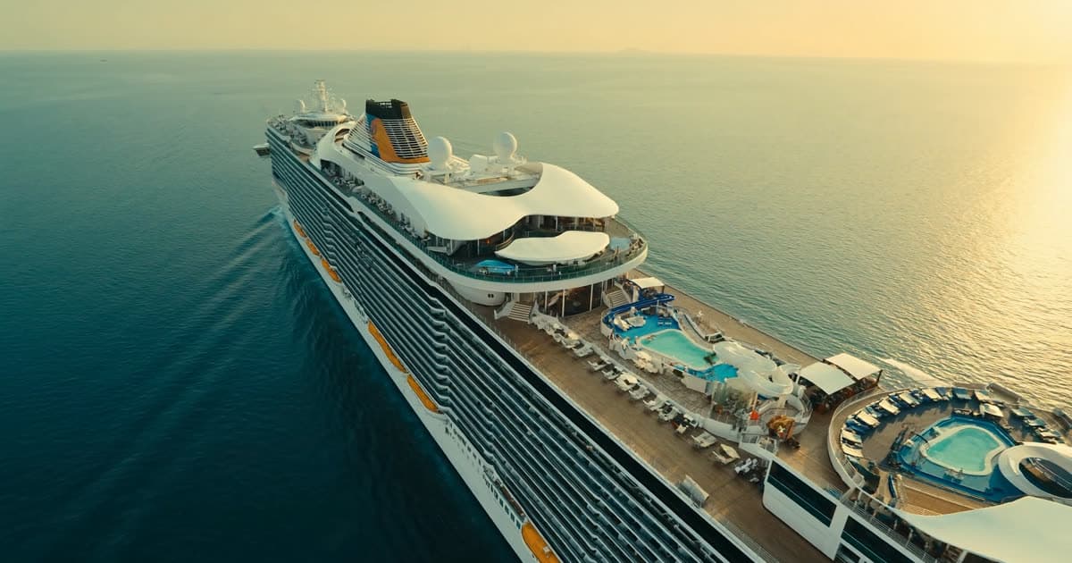 A large Royal Caribbean style cruise ship at sea under a warm evening sky