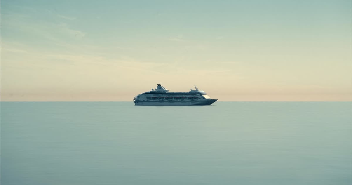A single cruise ship on a calm open sea under soft early-autumn light