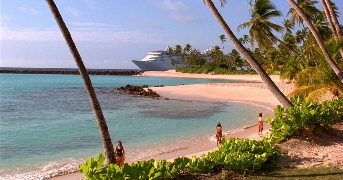 A cruise ship anchored off a turquoise Caribbean bay at sunset