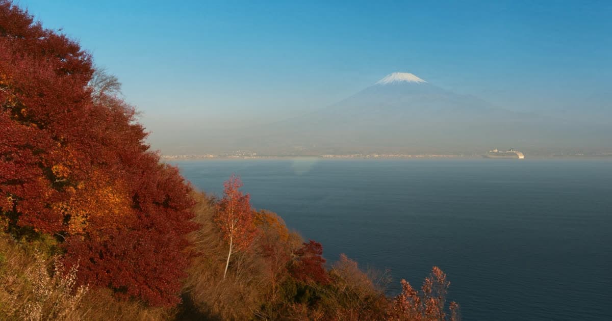 A cruise ship off a Japanese coastline with a distant volcanic peak