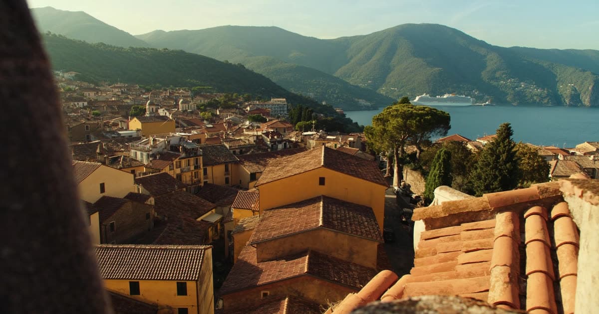 A cruise ship anchored beside a Mediterranean island town in warm evening light