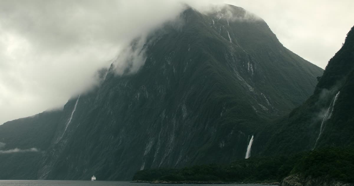 A cruise ship in a steep New Zealand fiord with waterfalls and low cloud