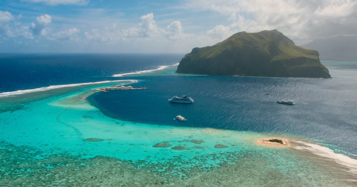 A small cruise ship inside a South Pacific lagoon ringed by a coral reef
