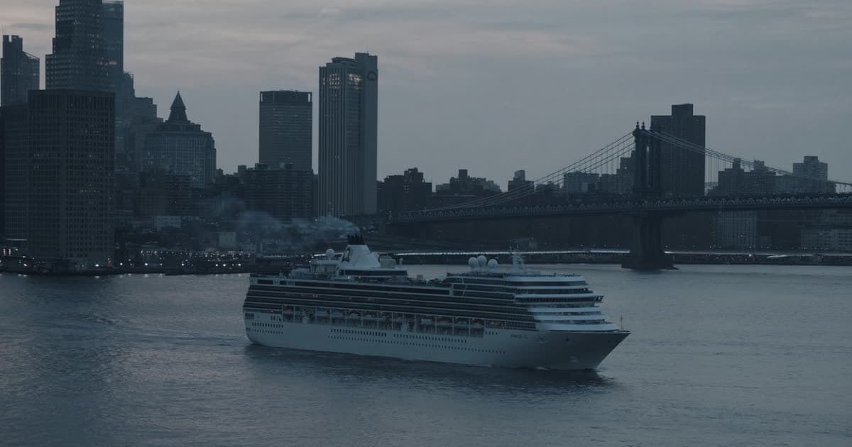 A cruise ship departing New York harbour past a city skyline at dusk