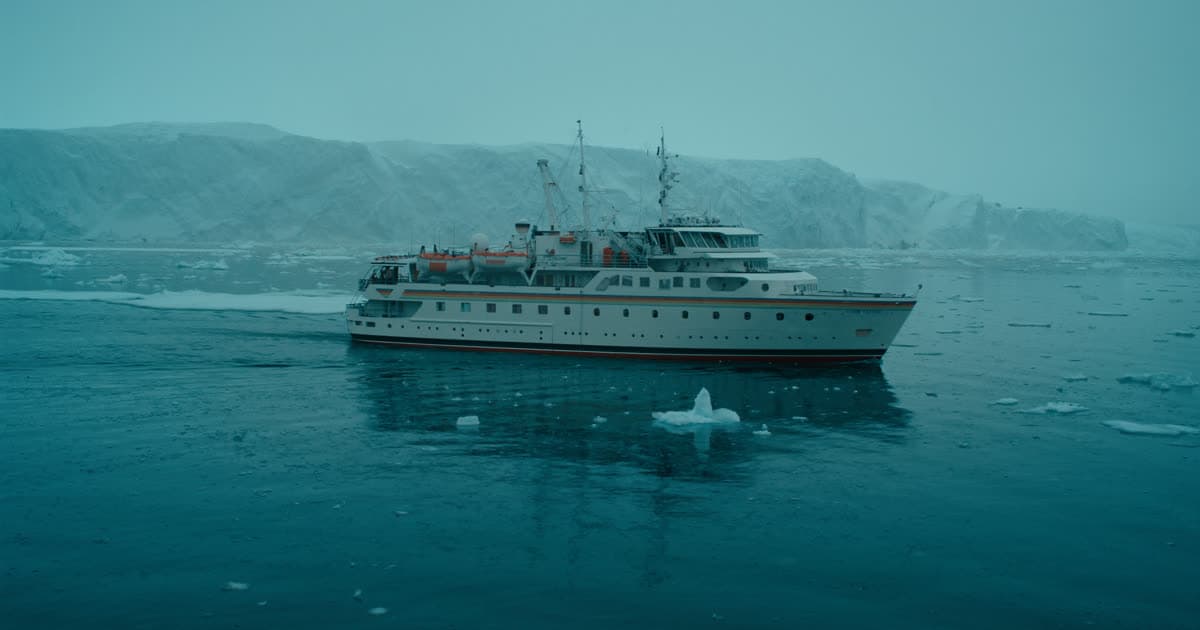 A Silversea style luxury ship in polar waters beside an ice-strewn shoreline
